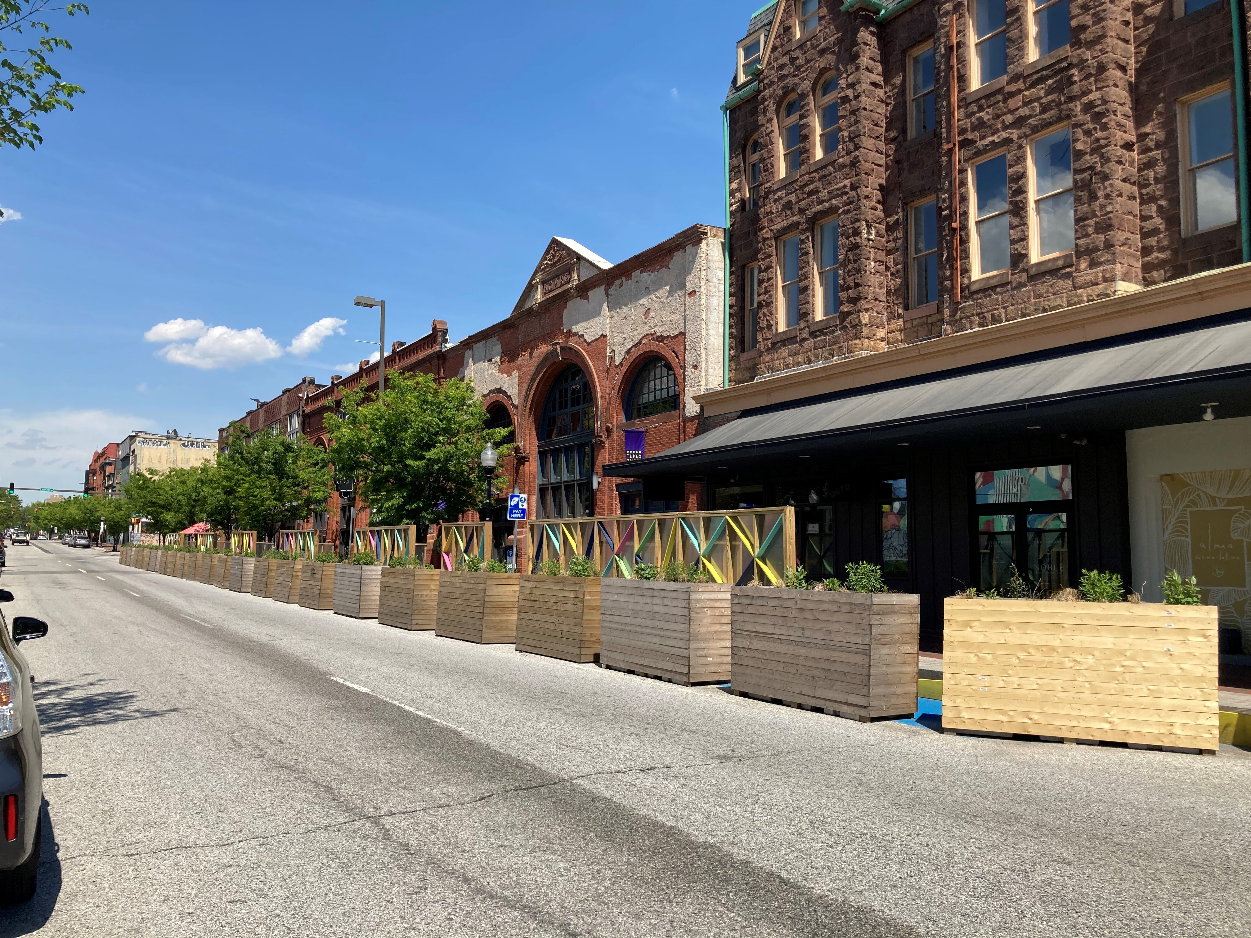 Planters and traffic barriers being used to protect parklet spaces within the roadway along a city block.